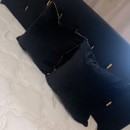 MS Glamour Usługi tapicerskie - Czarne poduszki z lamówką na białym materacu i ciemnym wezgłowiu z dekoracyjnymi przeszyciami. Ujęcie z góry, lekko obrócone.