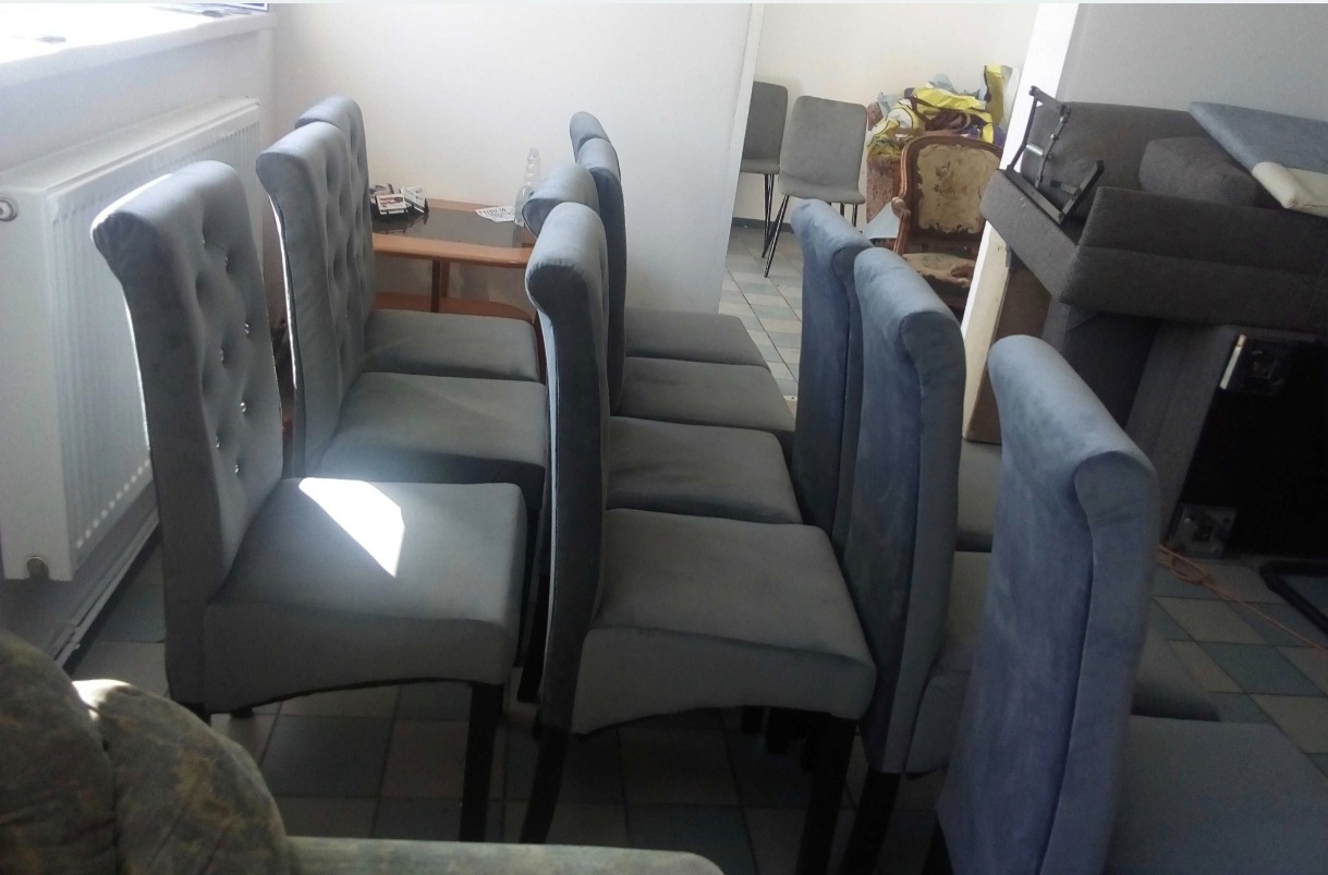 Rząd krzeseł tapicerowanych szarą tkaniną z ozdobnymi guzikami na oparciach, ustawionych w pomieszczeniu z meblami w tle.