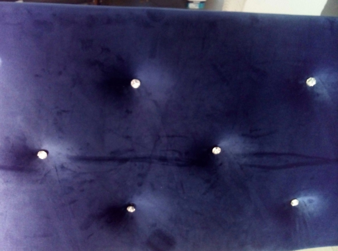 Granatowy, aksamitny zagłówek łóżka z dekoracyjnymi kryształkami, równomiernie rozmieszczonymi. Widoczne delikatne ślady użytkowania na tkaninie.