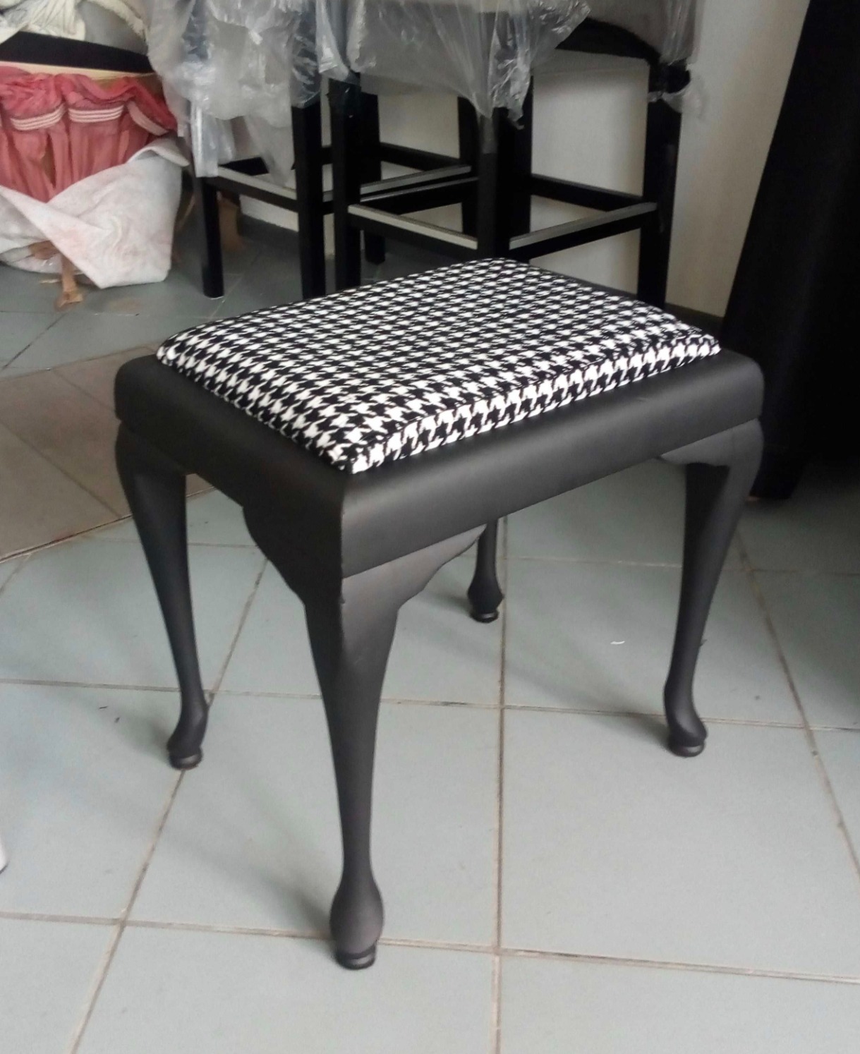 Odnowiony taboret w stylu retro z czarnymi nogami i siedziskiem w pepitkę. Widoczne detale toczonych nóg i staranne wykończenie tapicerki.