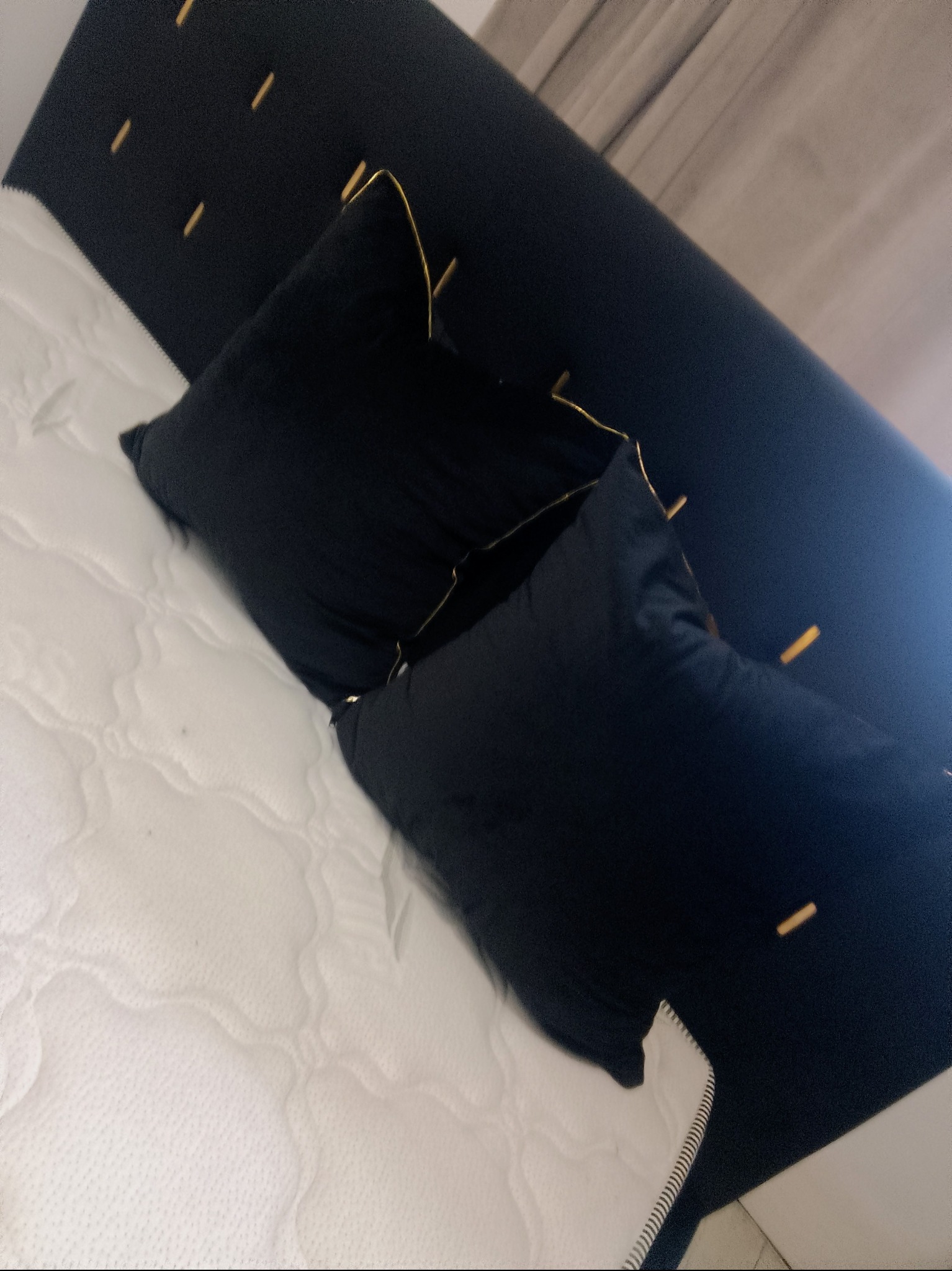 Czarne poduszki z lamówką na białym materacu i ciemnym wezgłowiu z dekoracyjnymi przeszyciami. Ujęcie z góry, lekko obrócone.