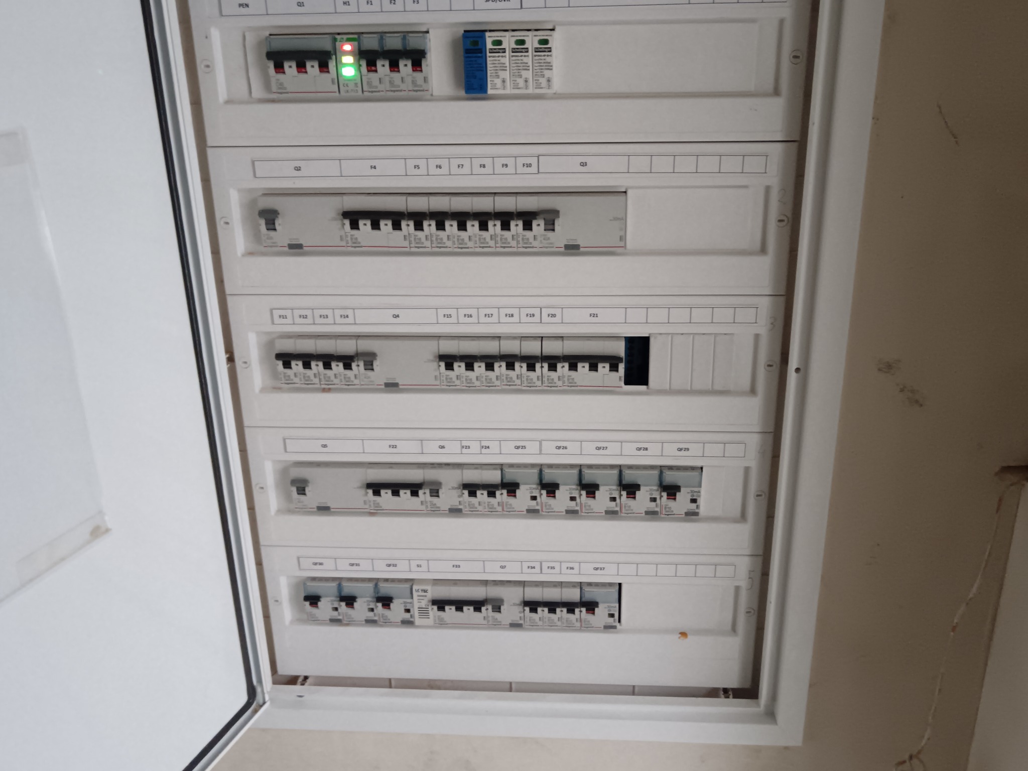 Rozdzielnica elektryczna z bezpiecznikami, widok z bliska. Otwarta obudowa ukazuje liczne zabezpieczenia i oznaczenia. Widoczne diody sygnalizacyjne.