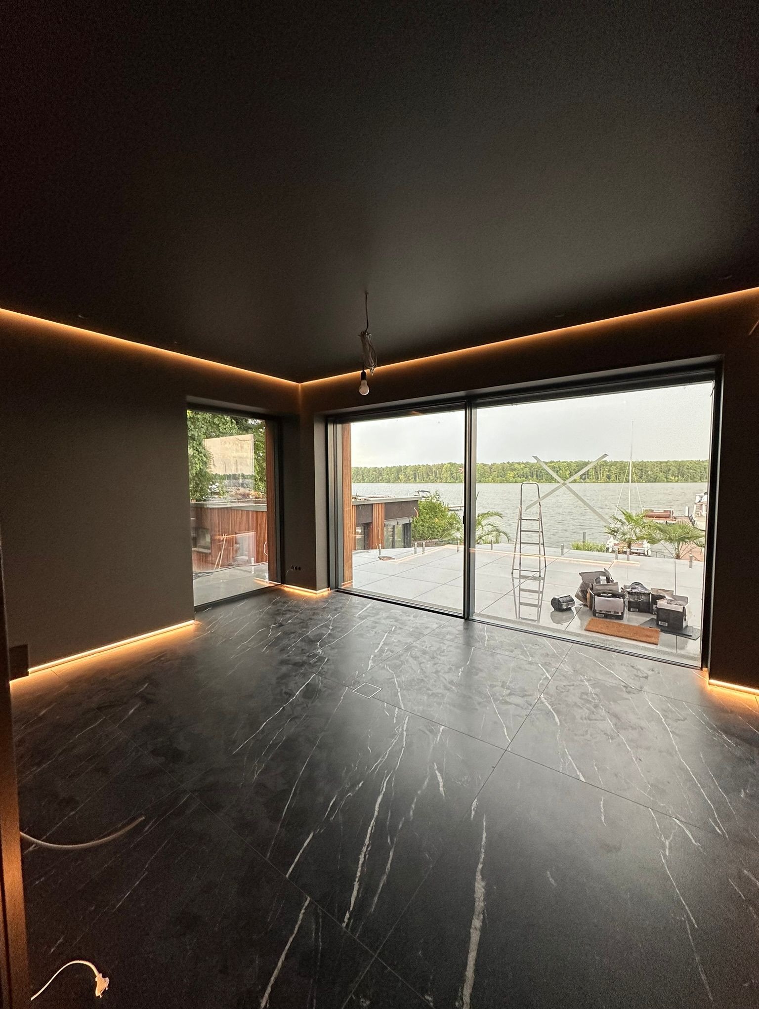 Nowoczesne wnętrze z czarną marmurową podłogą i subtelnym oświetleniem LED wzdłuż sufitu i podłogi. Widok na jezioro przez duże okno.
