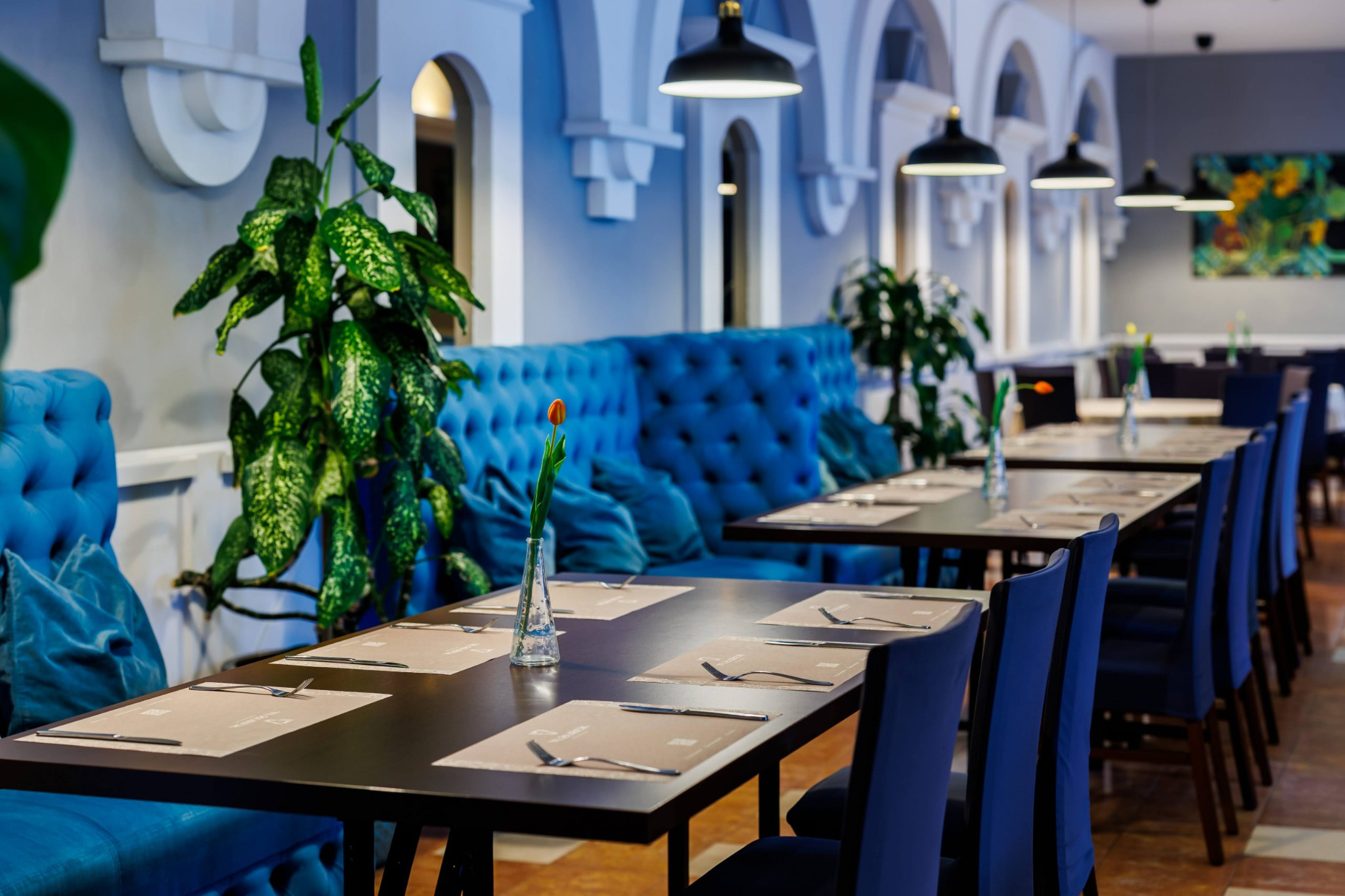 Elegancka sala bankietowa w Krakowie z turkusowymi sofami i nakrytymi stołami, gotowa na przyjęcie gości. Wazon z tulipanem dodaje uroku.