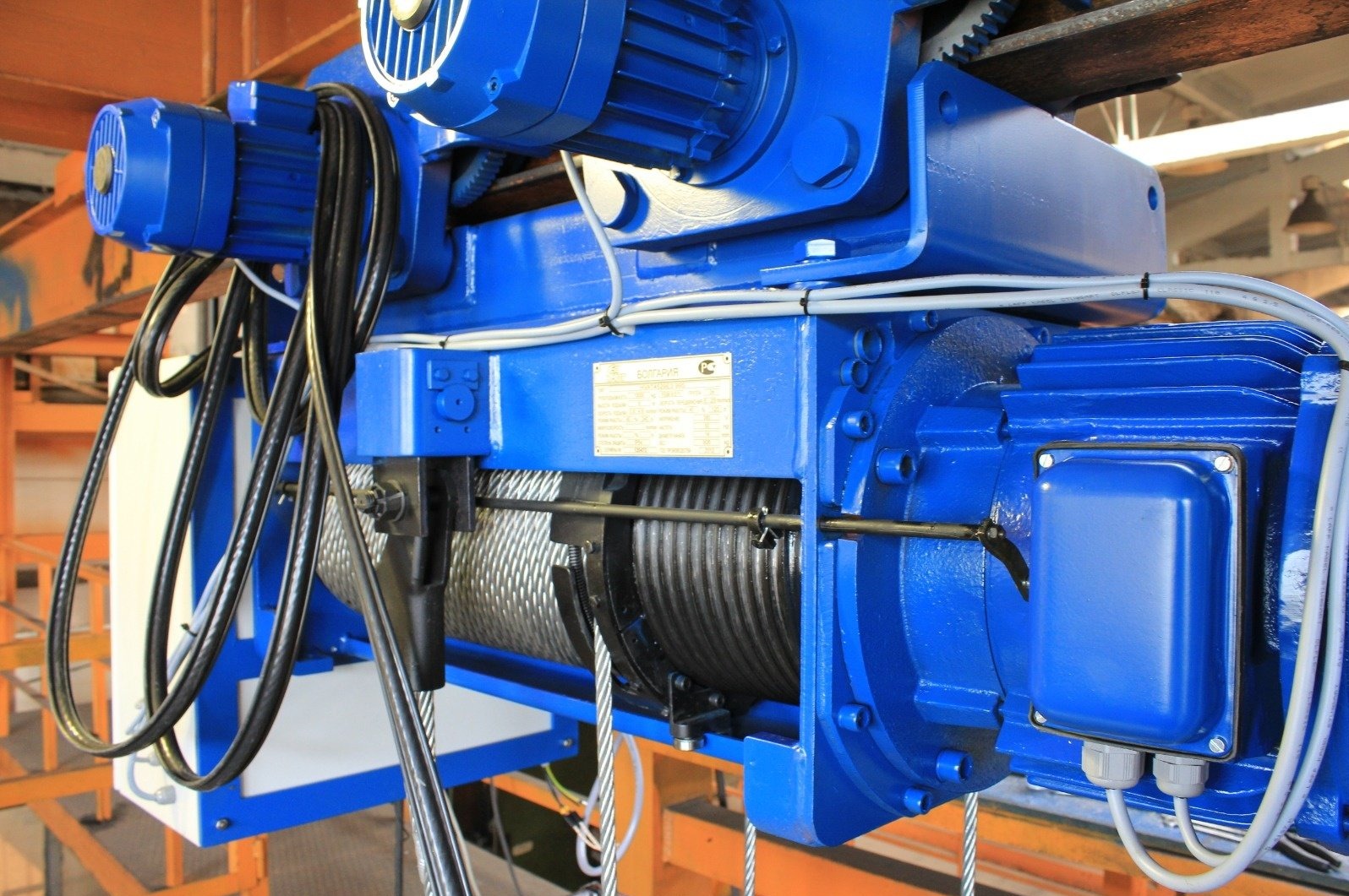Niebieski wciągnik linowy elektryczny z wózkiem jednoszynowym, widoczne silniki, liny i tabliczka znamionowa. Urządzenie przeznaczone do suwnic przemysłowych.