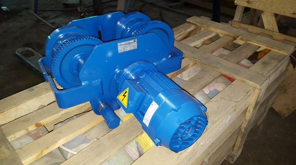 Niebieski wciągnik linowy ELMOT z silnikiem, na drewnianej palecie. Widoczne przekładnie zębate i tabliczka znamionowa. Urządzenie do transportu bliskiego w zakładach.