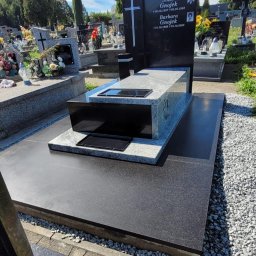 Nagrobki Śląsk - Czarny, nowoczesny nagrobek z jasnoszarym elementem, z wygrawerowanym krzyżem i zdjęciami zmarłych, na tle cmentarza w słoneczny dzień.