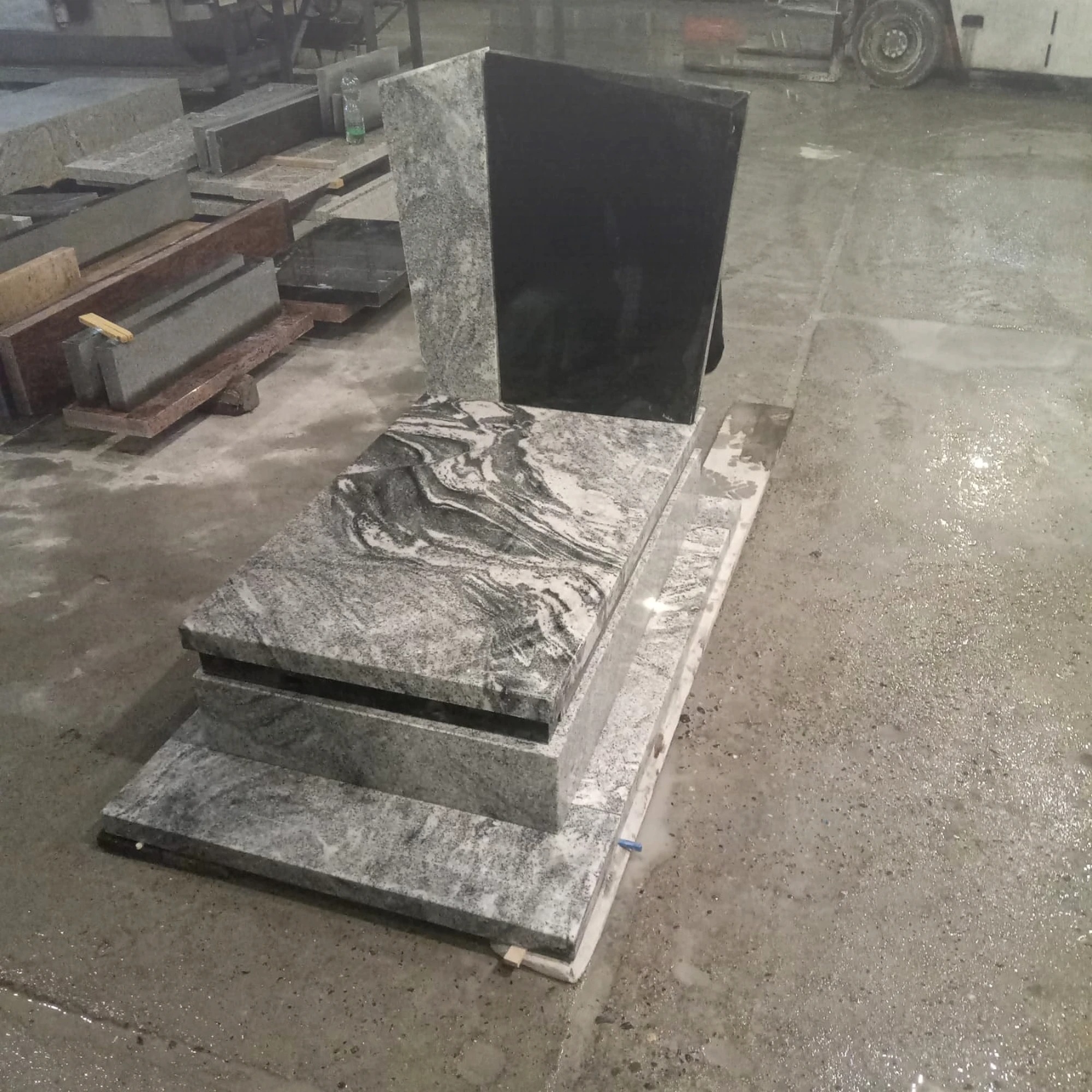 Gotowy, dwukolorowy pomnik z szarego i czarnego kamienia, z widocznym wzorem na płycie nagrobnej, ustawiony na mokrej posadzce w warsztacie kamieniarskim.