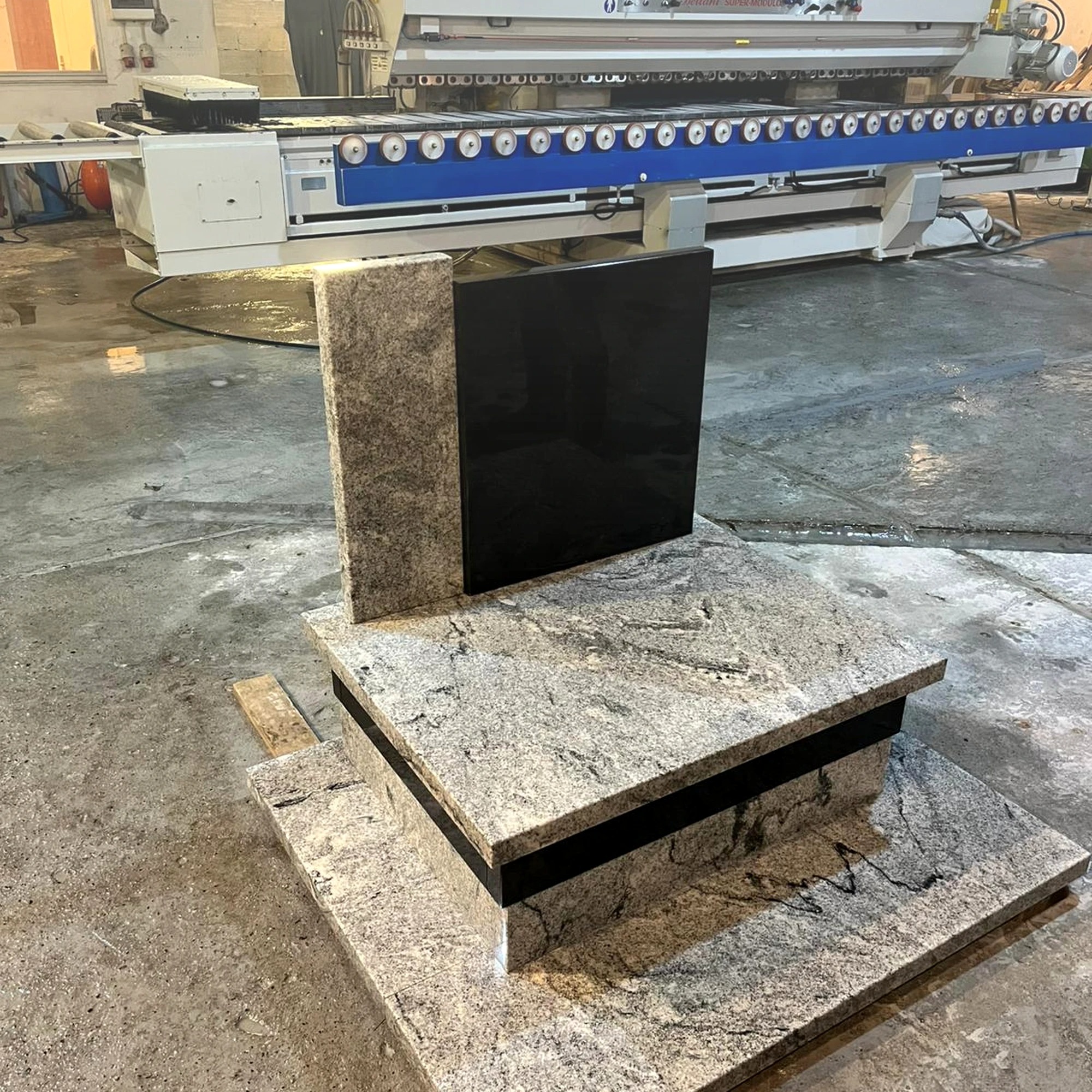 Surowy, granitowy nagrobek z czarną tablicą w Warszowicach, w tle maszyna kamieniarska. Widoczne ślady obróbki kamienia na posadzce.