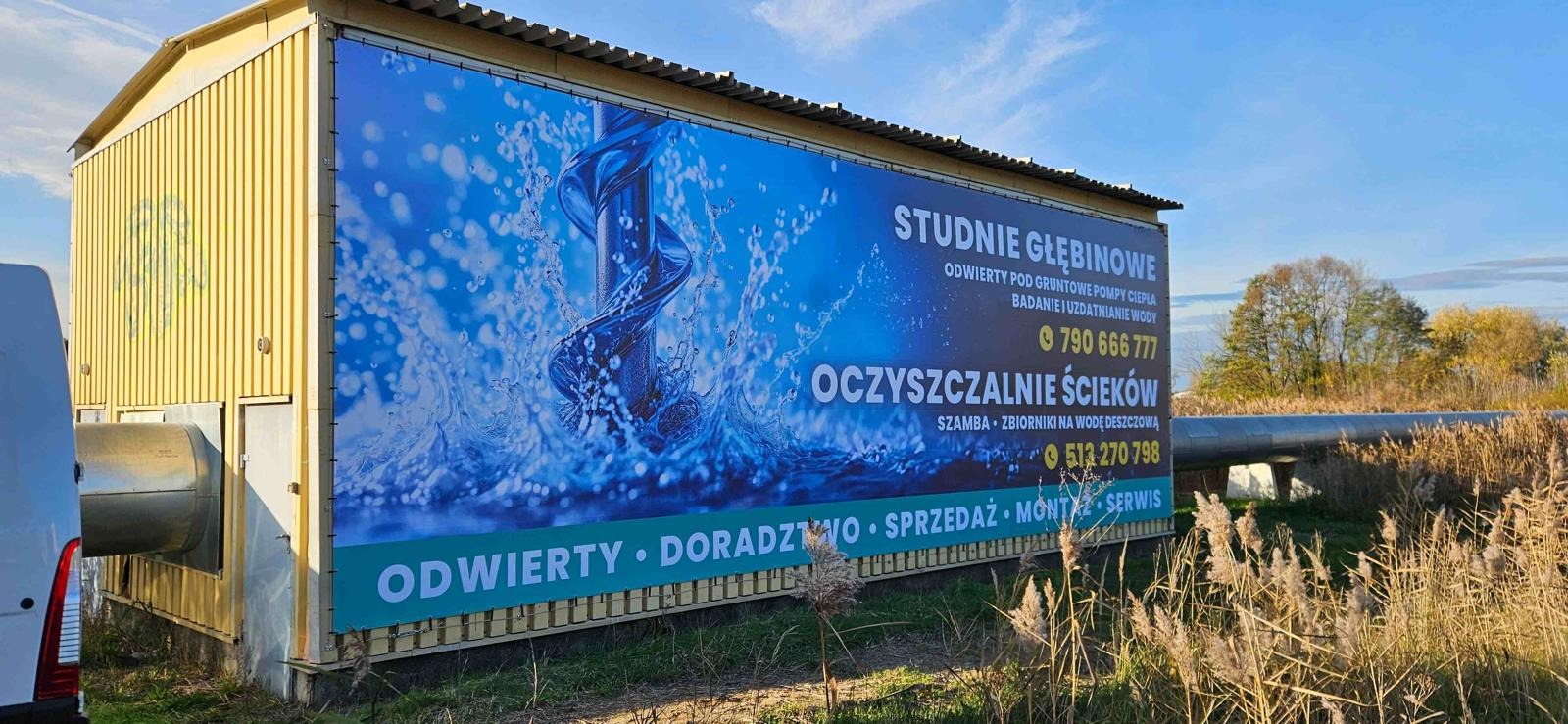 Reklama na przyczepie: studnie głębinowe, oczyszczalnie ścieków. Odwierty, doradztwo, sprzedaż, montaż, serwis. Grafika w niebieskich barwach z wiertłem i wodą.