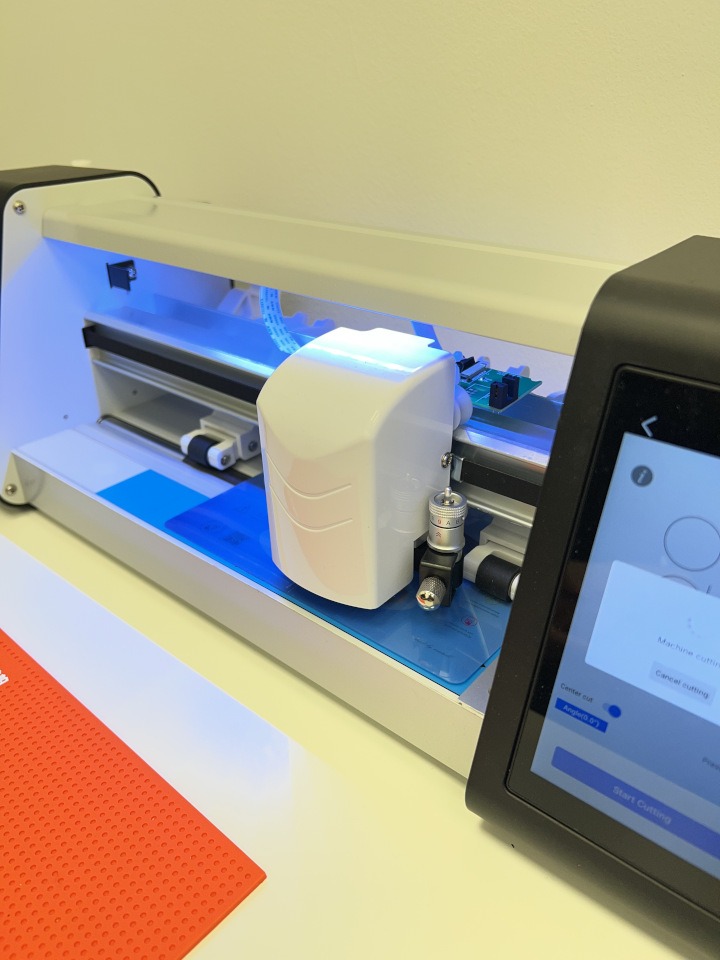 Plotter tnący z ekranem dotykowym, gotowy do precyzyjnego cięcia folii lub papieru. Podświetlenie LED podkreśla detale. Widoczny interfejs z opcjami cięcia.