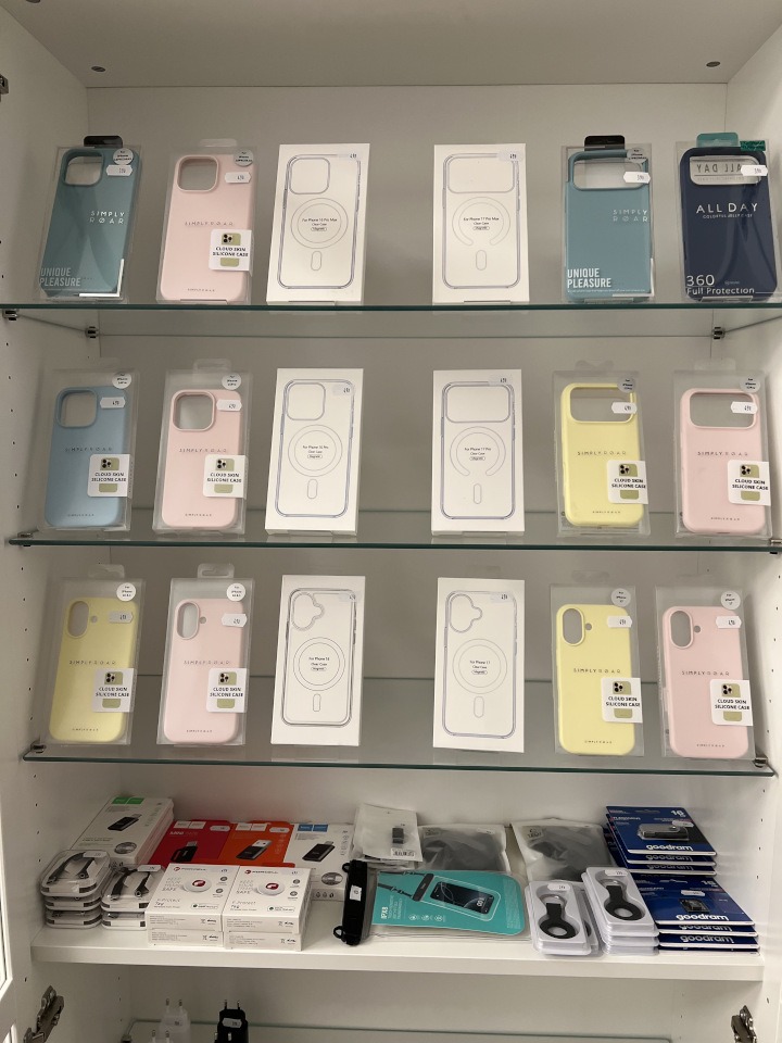 Półki z akcesoriami do telefonów: etui silikonowe w pastelowych kolorach, ładowarki i uchwyty. Widoczne opakowania z oznaczeniami i cenami.