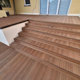 Bartosz Jedr - Wykończony taras z kompozytowych desek w odcieniach brązu, prowadzący schodami do drzwi balkonowych. Widoczne detale montażu i struktura desek.