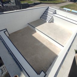 Firma Usługowa Raupe Daniel Gąsienica - Nowoczesny, betonowy basen w trakcie budowy, z widocznymi schodami i wykończeniami w kolorze białym i czarnym. Widok z góry, oświetlenie słoneczne.