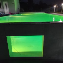 Firma Usługowa Raupe Daniel Gąsienica - Nocny widok na basen z podświetleniem LED, woda oświetlona na zielono, widoczne lampy oświetlające teren wokół basenu, nowoczesny design.
