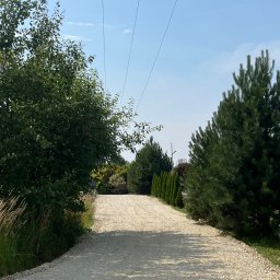 JB Nawierzchnie SP. Z o.o. - Żwirowa droga dojazdowa w Zabrzu, otoczona zielenią drzew i krzewów. Widok w perspektywie, z liniami energetycznymi nad drogą.