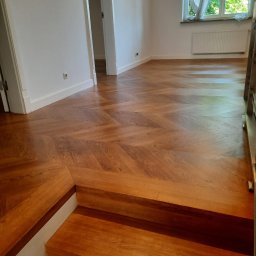 pro-desk-park - Parkiet ułożony we wzór jodełki francuskiej, widok z góry na schody drewniane. Jasne wnętrze z oknem i białymi ścianami. Detal wykończenia podłogi.