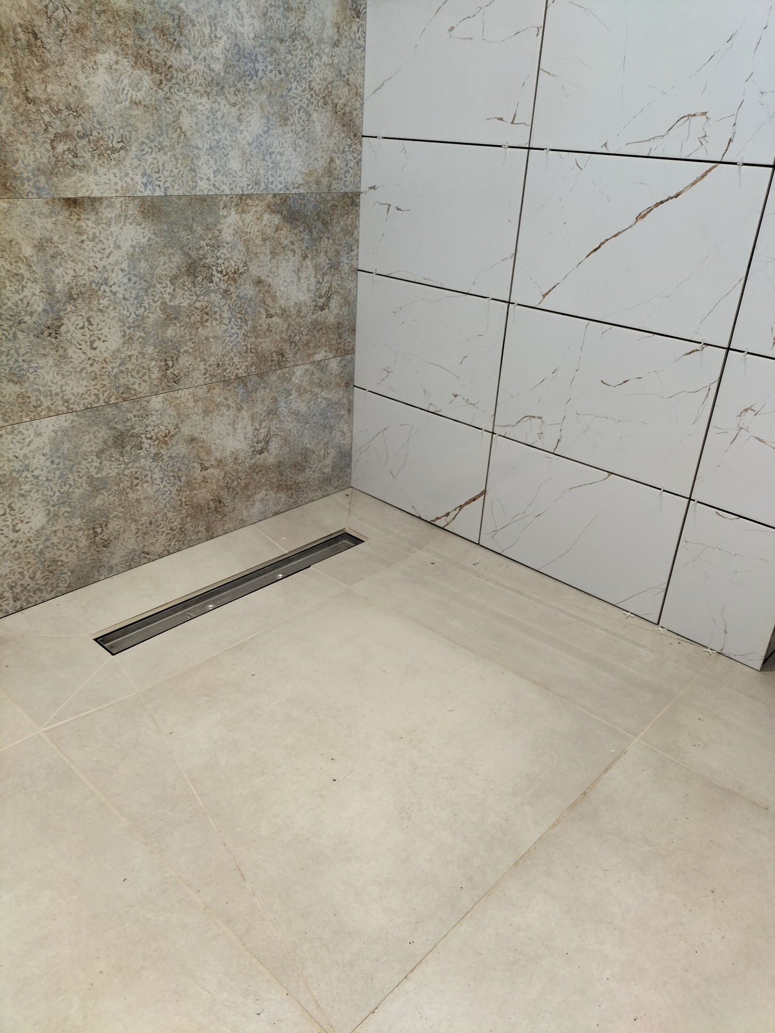 Wykończona łazienka z odpływem liniowym i płytkami imitującymi marmur na ścianach. Widoczne krzyżyki dystansowe między płytkami.