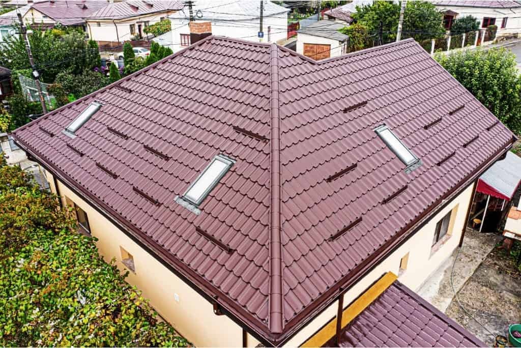Ciemnobrązowy dach z dachówki modułowej z dwoma oknami dachowymi, widok z góry na dom otoczony zielenią.