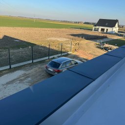 Fach plaski dach - Nowoczesny, płaski dach w kolorze antracytowym, z widocznym fragmentem elewacji domu w tle. Ujęcie z góry, podkreślające geometrię i minimalistyczny design.