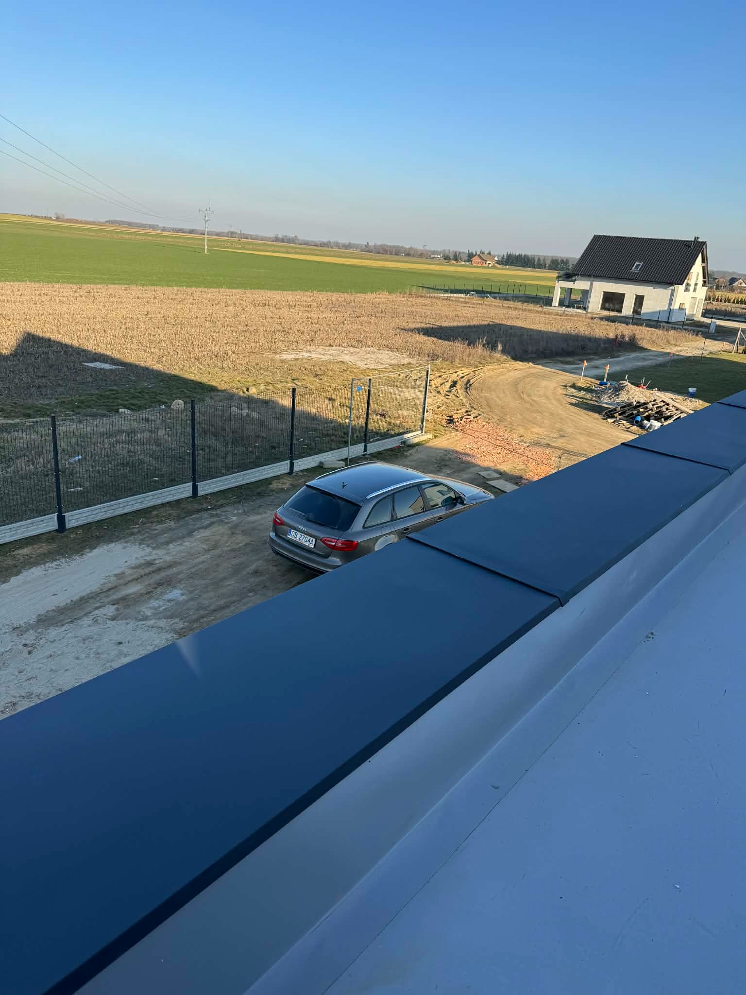 Nowoczesny, płaski dach w kolorze antracytowym, z widocznym fragmentem elewacji domu w tle. Ujęcie z góry, podkreślające geometrię i minimalistyczny design.