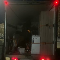 Yurii Herych - Wnętrze załadowanego busa transportowego: meble, pralka Electrolux i inne przedmioty zabezpieczone pasami. Widoczne światła stopu i oświetlenie wewnętrzne.