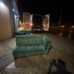 Yurii Herych - Turkusowa sofa chesterfield na chodniku, otwarte drzwi busa w tle. Nocna sceneria, mokra nawierzchnia. Nietypowe ujęcie mebla przed transportem.