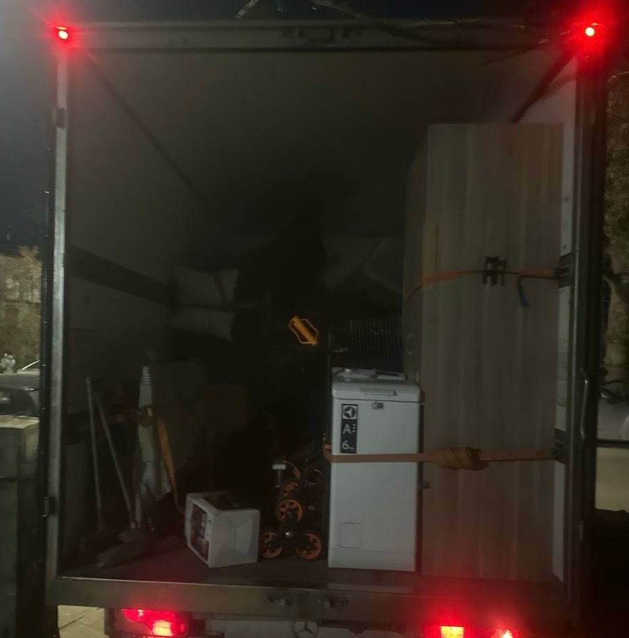 Wnętrze załadowanego busa transportowego: meble, pralka Electrolux i inne przedmioty zabezpieczone pasami. Widoczne światła stopu i oświetlenie wewnętrzne.