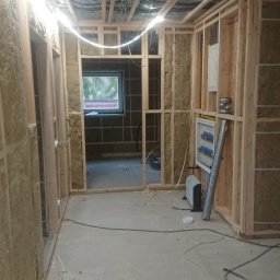 Adrian Węgrecki - Wnętrze w trakcie remontu: drewniana konstrukcja ścian z izolacją, widoczne instalacje elektryczne i wentylacyjne, surowy beton na podłodze. Etap prac wykończeniowych.