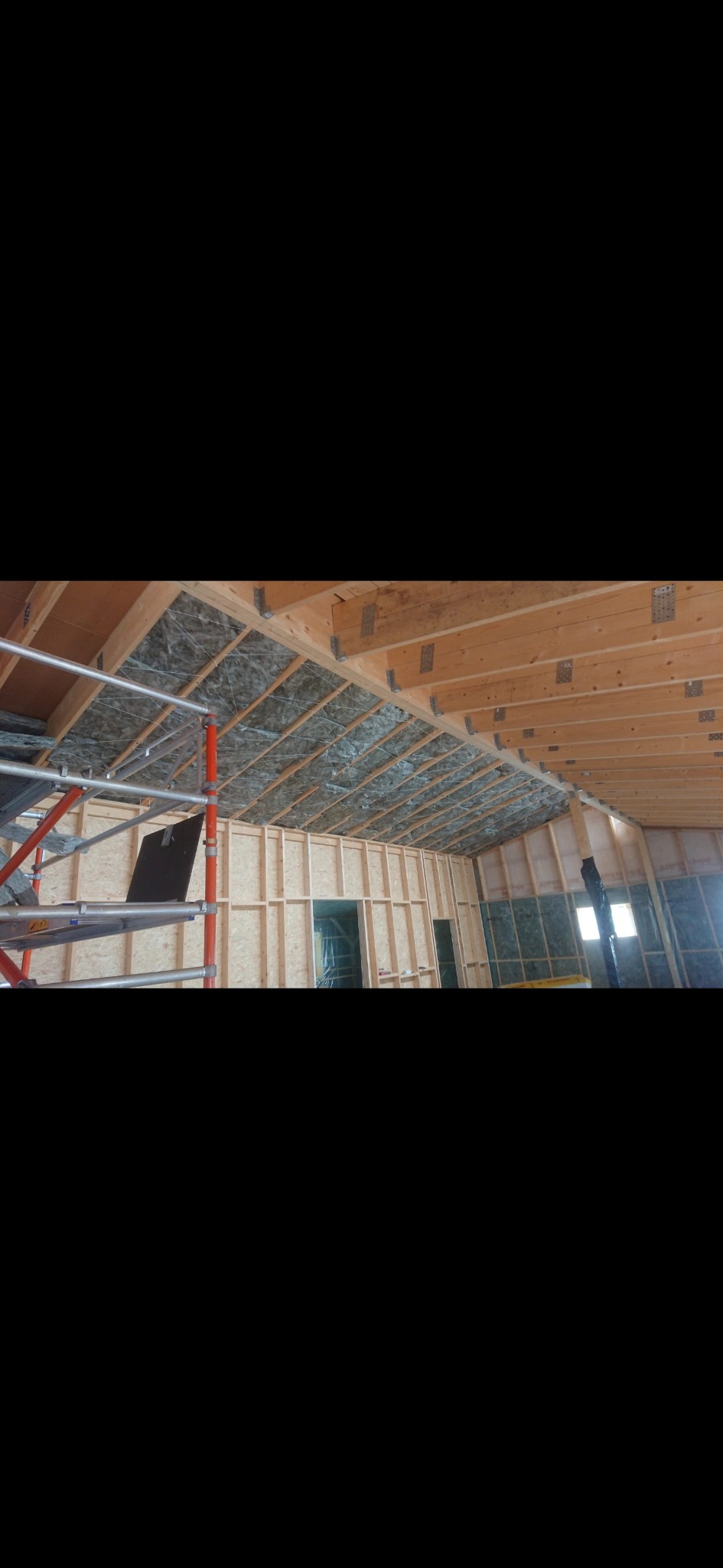 Wnętrze w trakcie prac wykończeniowych: ocieplony strop, ściany z płyt OSB, rusztowanie. Widoczne okna i elementy konstrukcyjne dachu.