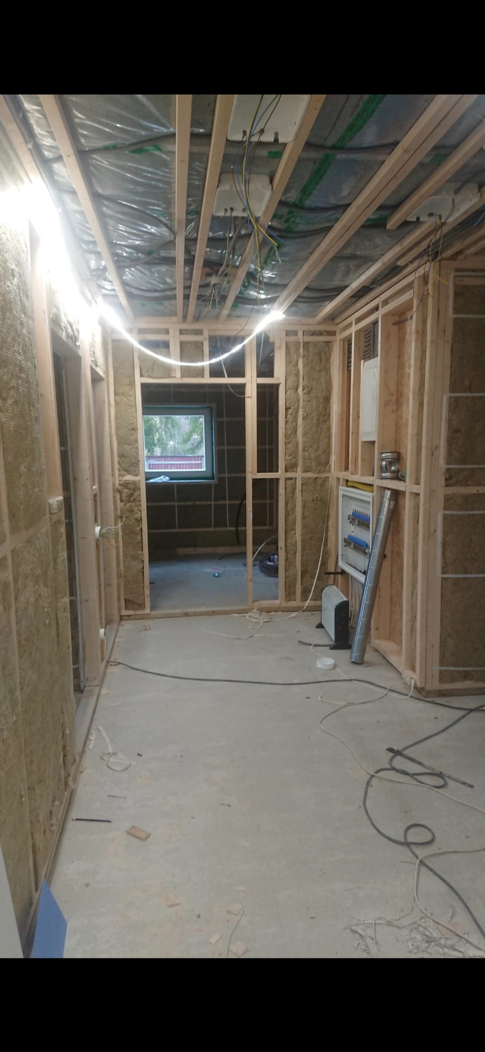 Wnętrze w trakcie remontu: drewniana konstrukcja ścian z izolacją, widoczne instalacje elektryczne i wentylacyjne, surowy beton na podłodze. Etap prac wykończeniowych.