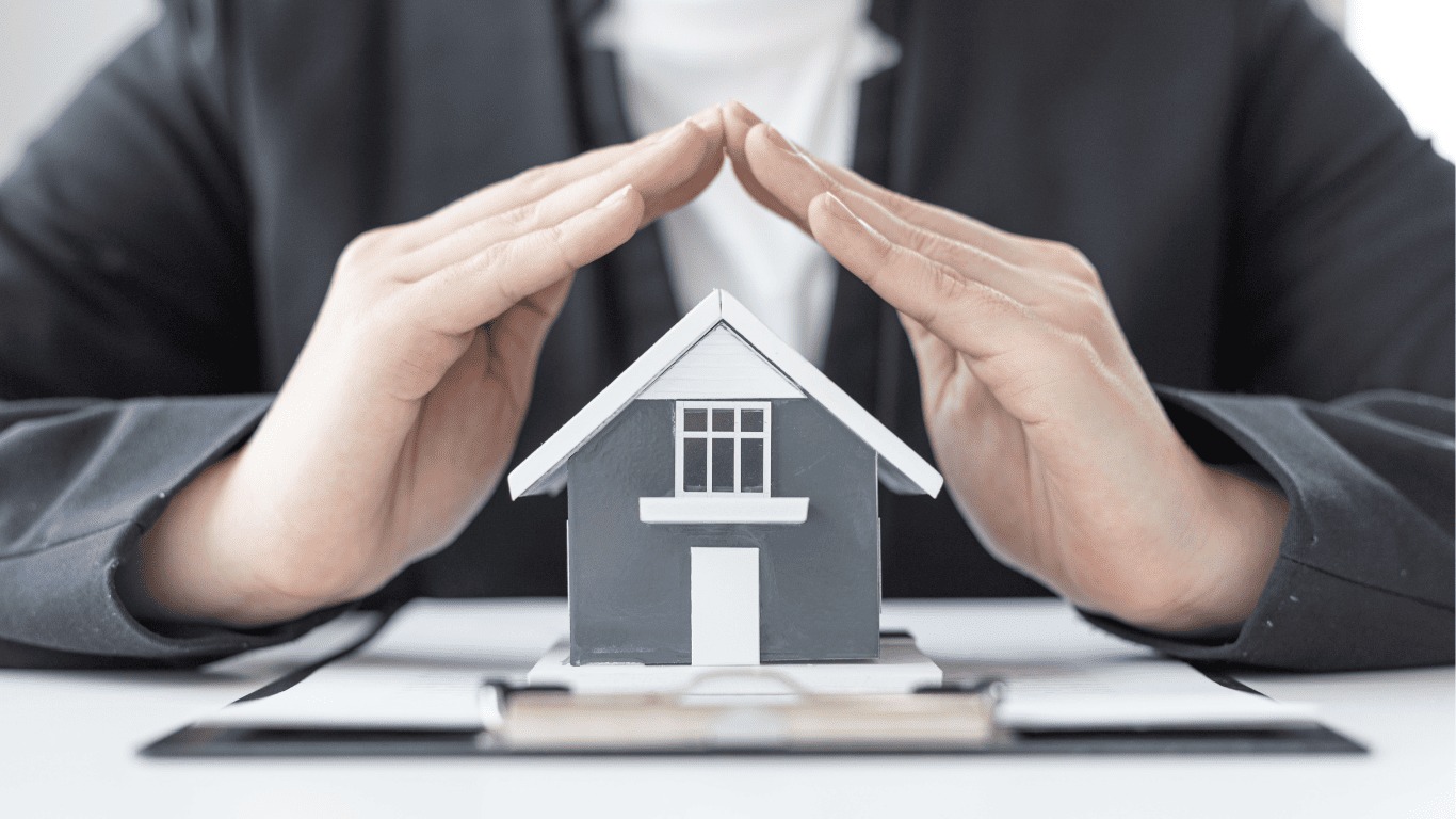 Model domu chroniony dłońmi na dokumencie. Bezpieczeństwo nieruchomości, ochrona inwestycji, polisa ubezpieczeniowa. Neutralne tło, biznesowy charakter.