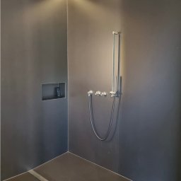 Nowoczesna kabina prysznicowa w ciemnej tonacji z oświetleniem LED, chromowaną armaturą i wnęką na kosmetyki. Minimalistyczny design z odpływem liniowym.