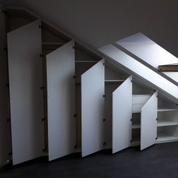 JUST.LUXURY BARBARA GROBLICKA, MONIKA GÓRNIAK-SEROWIK S.C. - Biała szafa wnękowa na poddaszu ze skośnym sufitem, otwarte drzwi ukazują półki i drążki. Widoczne okno dachowe i grzejnik. Ciemna podłoga.