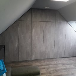 JUST.LUXURY BARBARA GROBLICKA, MONIKA GÓRNIAK-SEROWIK S.C. - Szafa wnękowa na poddaszu ze skośnym sufitem, szare fronty z efektem betonu, widoczne okno dachowe i fragment podłogi z dekoracyjnym wzorem.