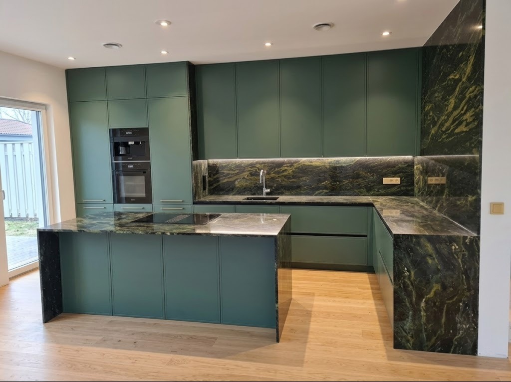 Nowoczesna kuchnia w odcieniach zieleni z wyspą i blatem z kamienia naturalnego. Minimalistyczne fronty szafek, oświetlenie LED podszafkowe, sprzęt AGD w zabudowie.