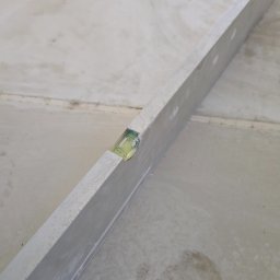 Fine Space Remonty - Poziomica aluminiowa na szarej, betonowej posadzce. Widoczne łączenia płyt posadzkowych. Narzędzie ustawione ukośnie, sprawdzające równość powierzchni.