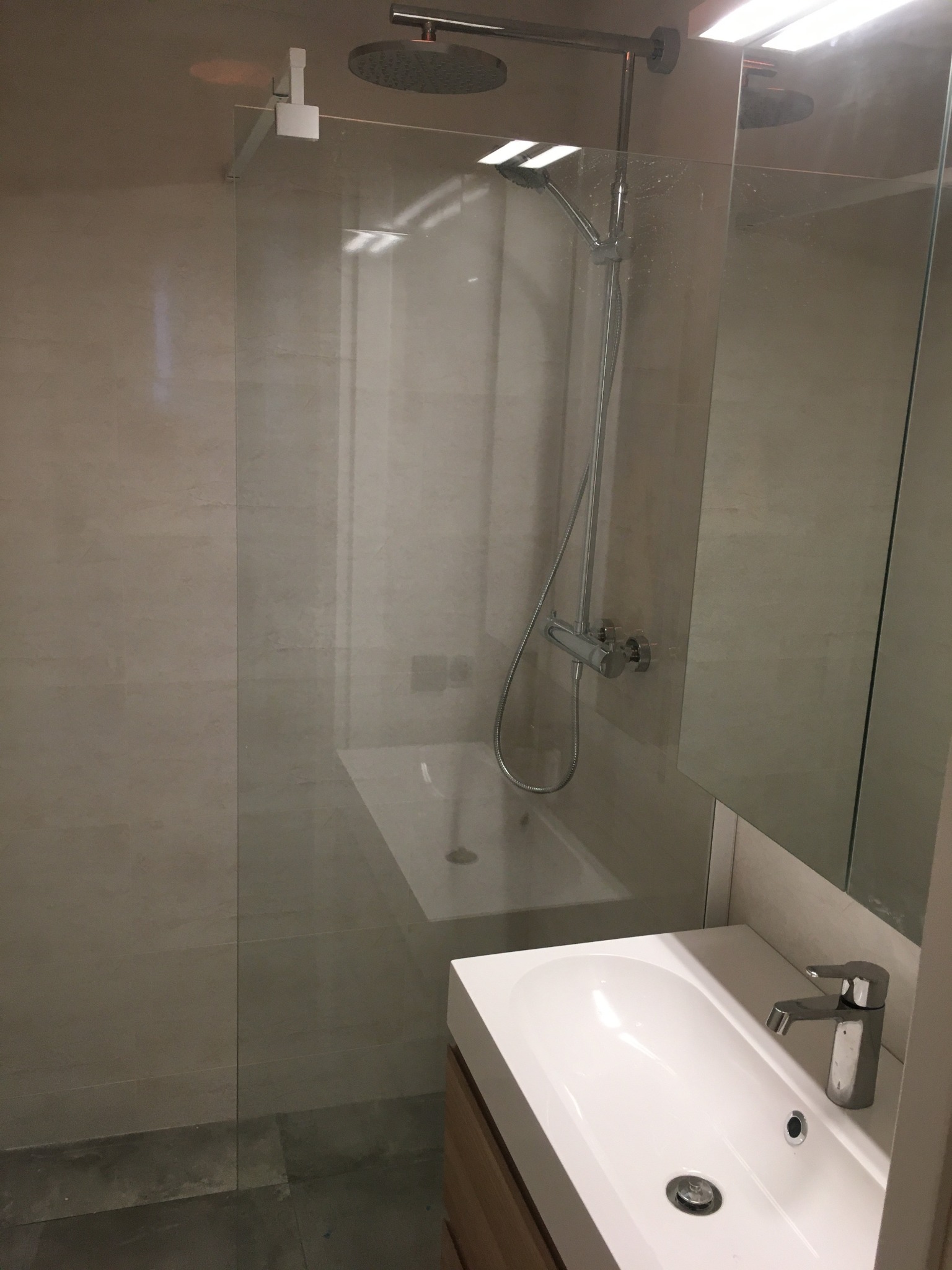 Nowoczesna łazienka z kabiną prysznicową typu walk-in, umywalką nablatową i dużym lustrem. Minimalistyczny design, jasne płytki, chromowana armatura.