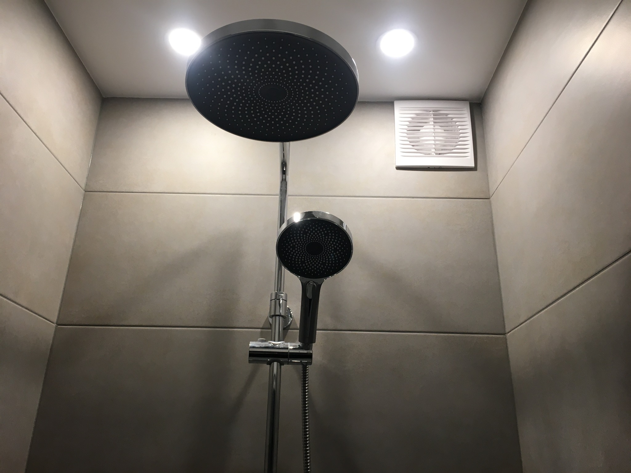 Nowoczesny zestaw prysznicowy z deszczownicą i wentylatorem w łazience wykończonej płytkami w odcieniach szarości. Minimalistyczny design, oświetlenie punktowe.