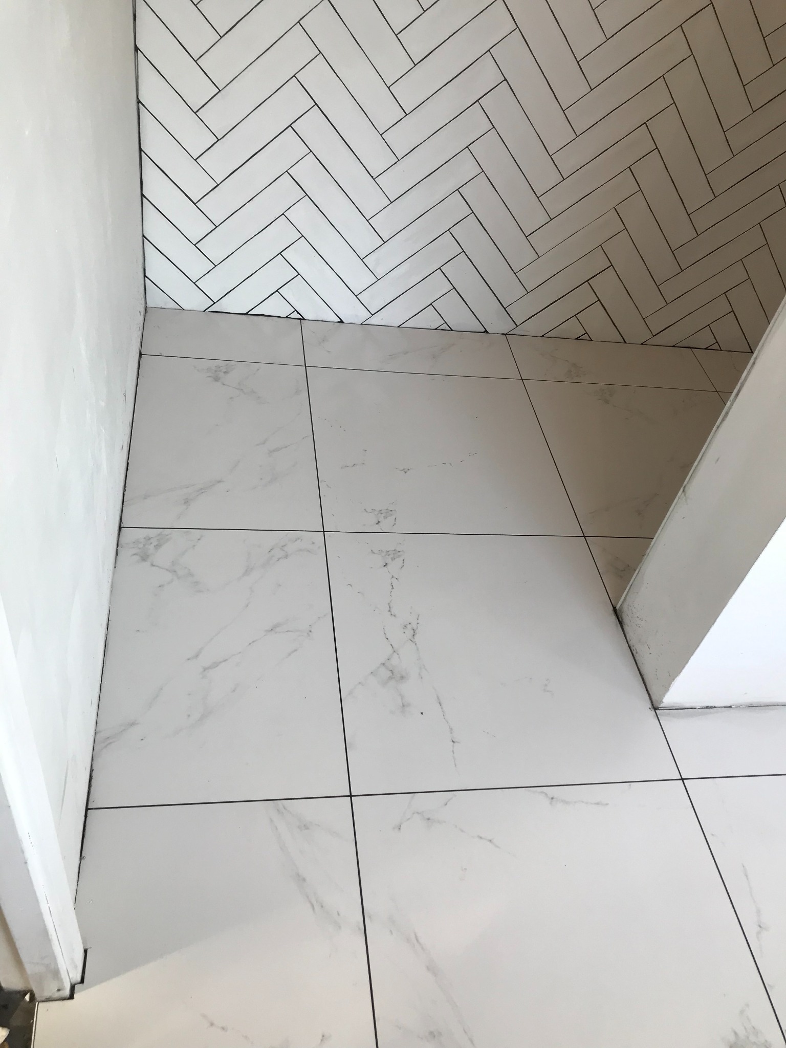 Białe, marmurowe płytki podłogowe i ściana z białej cegły ułożonej w jodełkę. Widok z góry, ukazujący precyzję wykonania i estetykę wykończenia łazienki.