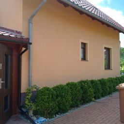 CleanRAT - Odnowiona elewacja domu jednorodzinnego w odcieniach beżu, z nową stolarką okienną i zadbanym otoczeniem. Widoczne detale: rynny, dachówka i kostka brukowa.