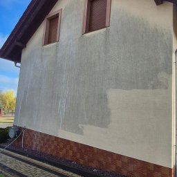 CleanRAT - Fragment elewacji domu z widocznymi śladami mycia i częściowo nałożoną farbą, ukazujący postęp prac. Widoczny sprzęt do mycia i fragment chodnika.