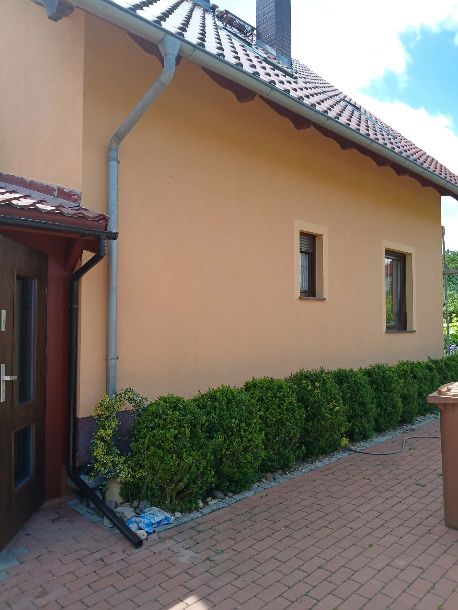 Odnowiona elewacja domu jednorodzinnego w odcieniach beżu, z nową stolarką okienną i zadbanym otoczeniem. Widoczne detale: rynny, dachówka i kostka brukowa.