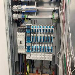 Konrad Hartmann - Rozdzielnia elektryczna z zainstalowanymi bezpiecznikami, licznikami i okablowaniem. Widoczne elementy montażowe i przewody w różnych kolorach.
