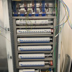 Konrad Hartmann - Rozdzielnica elektryczna z licznymi zabezpieczeniami i przewodami wewnątrz szafy, widok z bliska na zainstalowane komponenty i okablowanie.