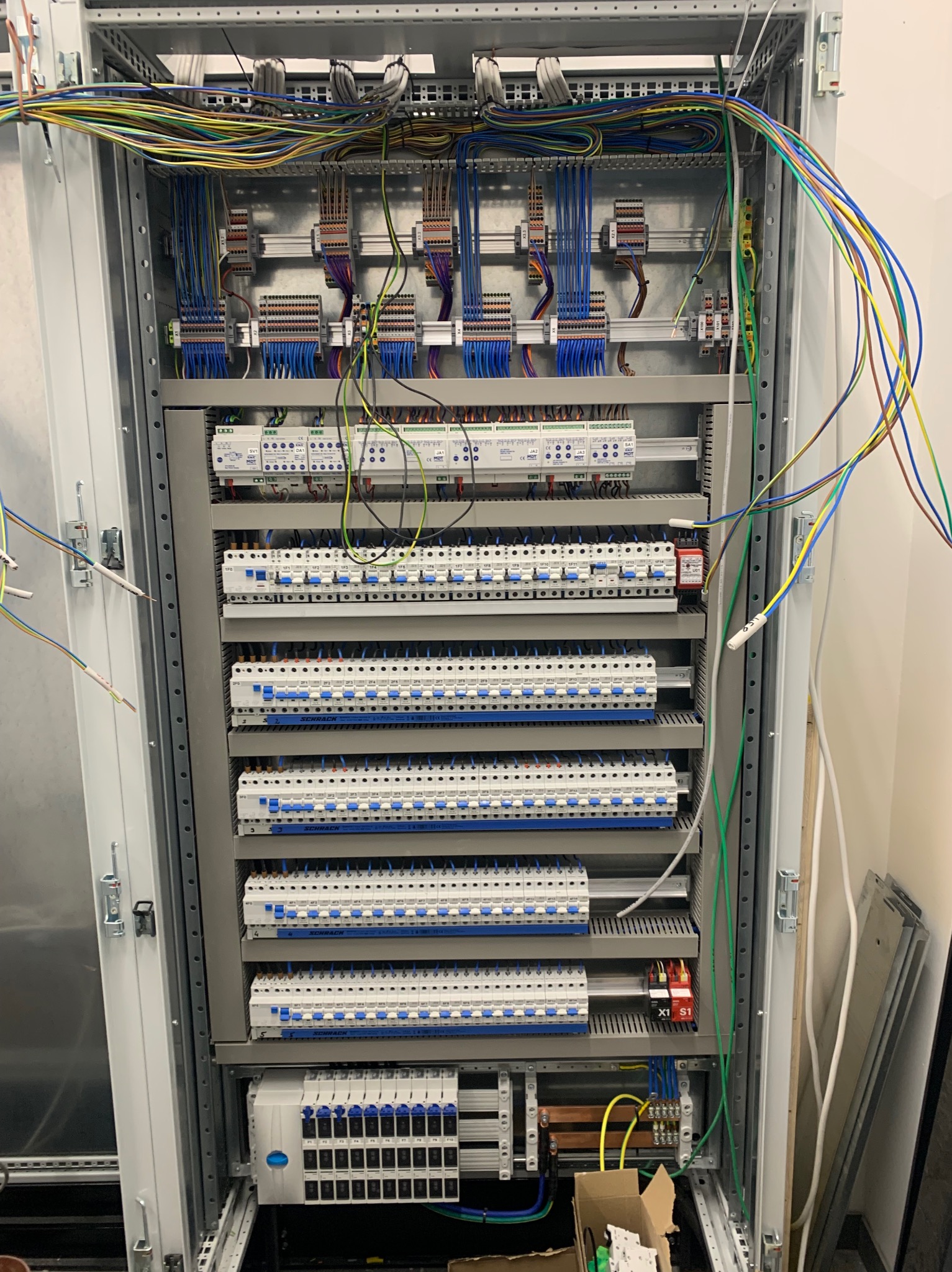 Rozdzielnica elektryczna z licznymi zabezpieczeniami i przewodami wewnątrz szafy, widok z bliska na zainstalowane komponenty i okablowanie.