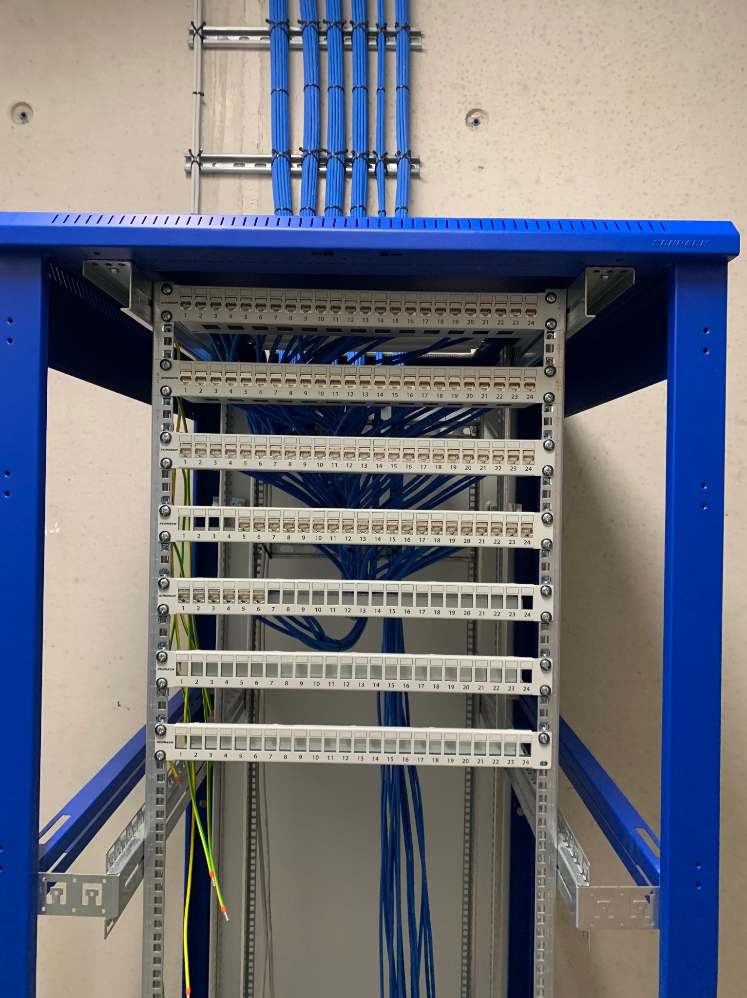 Rozdzielnica elektryczna w szafie rack z podłączonymi kablami. Widoczne złącza i uporządkowane przewody w kolorze niebieskim. Estetyczne wykonanie.
