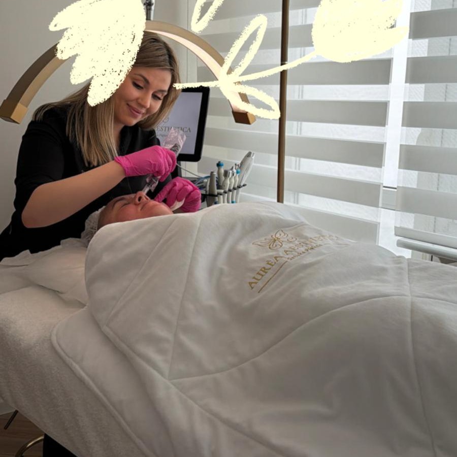 Klientka leży na łóżku zabiegowym, kosmetyczka w różowych rękawiczkach wykonuje zabieg na twarzy. Widoczne narzędzia i lampa zabiegowa.