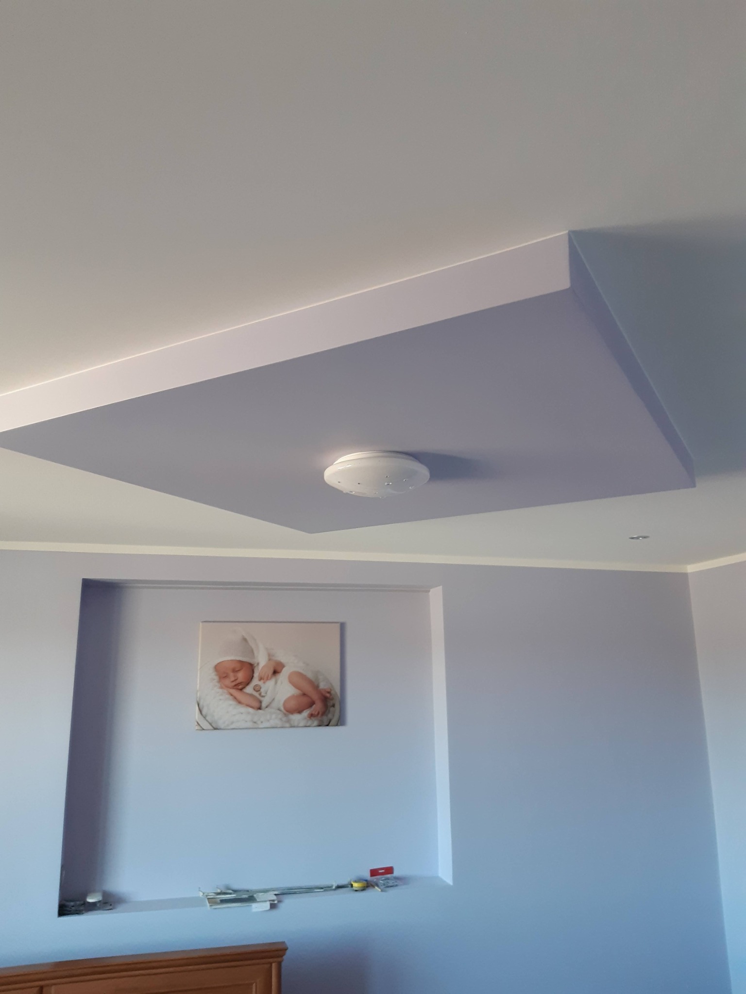 Podwieszany sufit w odcieniach fioletu z centralnym oświetleniem LED, dopasowany kolorystycznie do ścian i wnęki z obrazem dziecka. Nowoczesne wykończenie wnętrza.