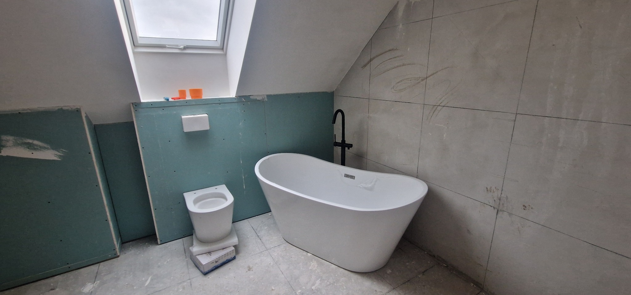 Wnętrze łazienki w trakcie wykończenia w Tarnowie. Widoczna wanna wolnostojąca, toaleta na podwyższeniu, płyty gipsowe i płytki na ścianach.